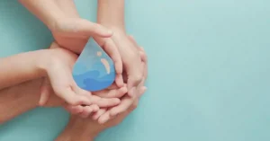A group of hands cradling a blue water droplet illustration, symbolizing unity and care for water conservation.