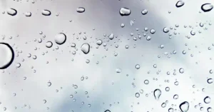 Close-up of raindrops on a transparent surface, with blurred gray clouds in the background creating a soft, soothing atmosphere.