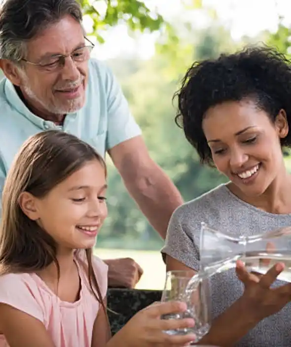 A happy woman pours fresh, clean water for happy girl surrounded by a man who is smiling in a sunny outdoor setting, showcasing the benefits of professional water treatment in Lehigh Acres.