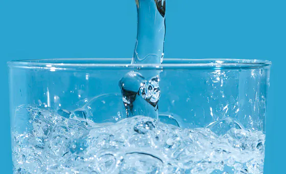 Close-up of a glass being filled with clear water, creating splashes against a bright blue background.