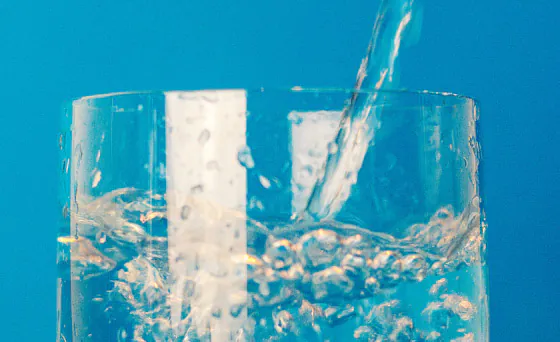 A glass closeup shot of being filled with clear water, creating splashes against a bright blue background. Crisp, filtered well water service in Lehigh Acres, FL, ensuring safe and refreshing hydration.
